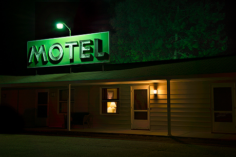Night Vision - A dirive-in motel at night located in Bloomer, Wisconsin. A single room lamp is visibly on while the motel sign overhead is alit humming a green-glowing light.